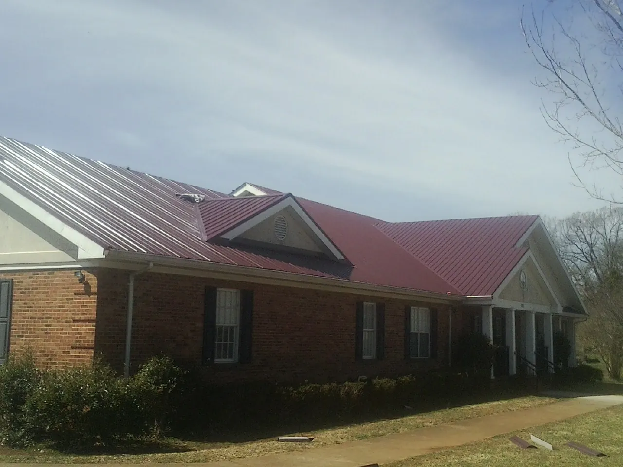 Red metal roof with gabled entries on a long brick building, from a Hail Damage Roof Repair job in Scotts Valley