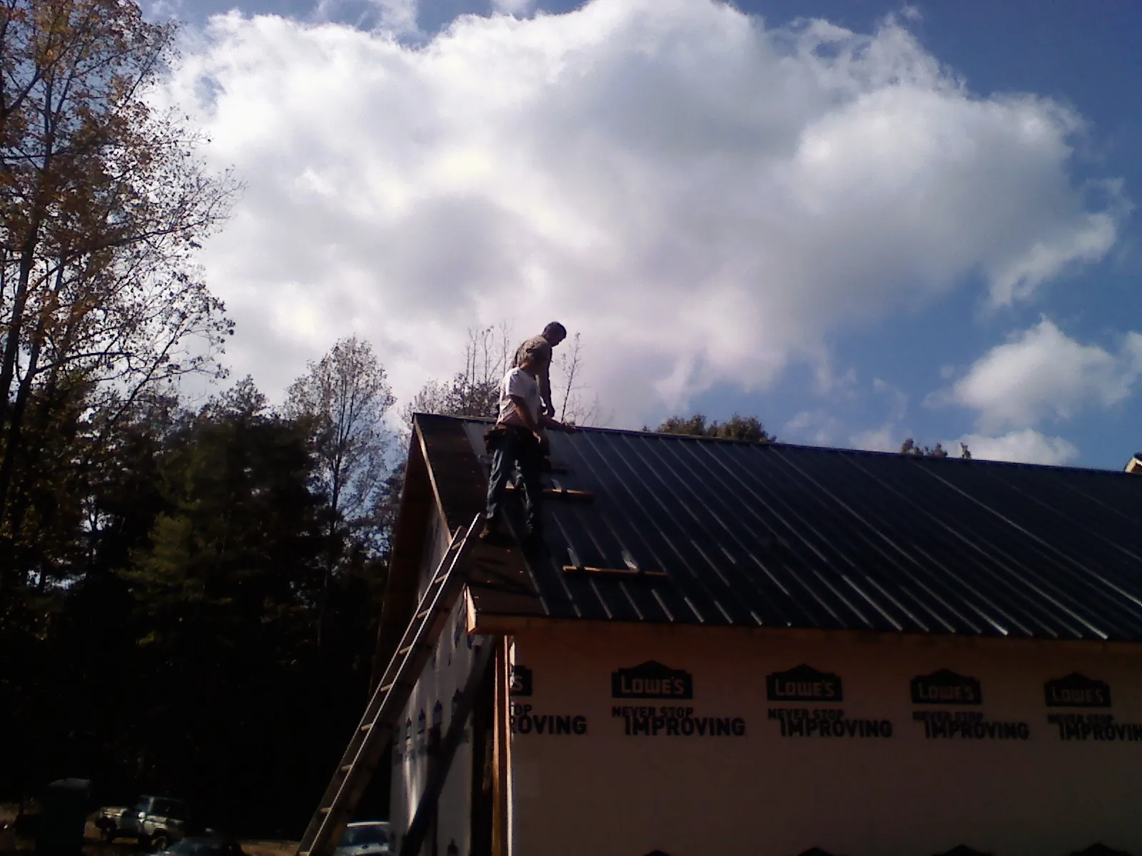 Roofer fastening dark metal panels high against a cloudy sky, from a Roof Inspection job in Scotts Valley