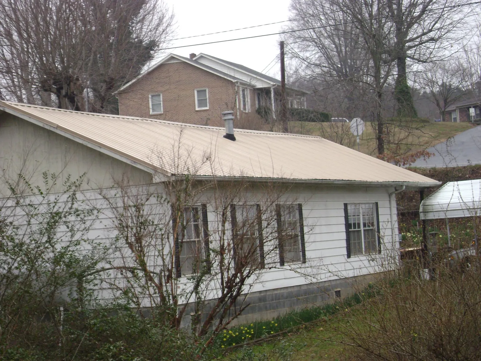 Tan metal roof on a white sided house set into a hillside — Commercial Roofing by Roofing Brothers in Scotts Valley